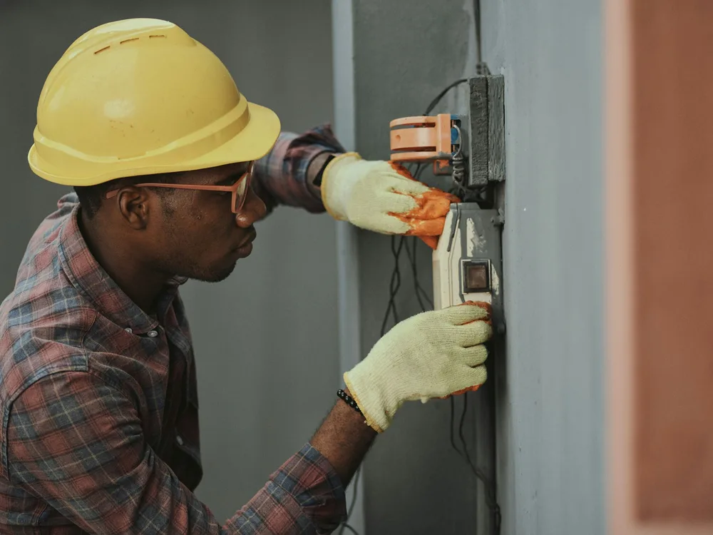 Electrician mounting a new electrical junction box on an exterior wall during a repair
